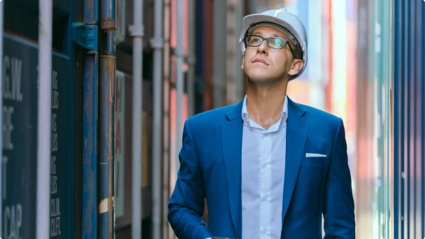 Homem com capacete de proteção andando entre containers.