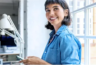 Jovem mulher branca, de cabelo curto e franja, sorrindo e olhando para o lado enquanto utiliza seu smartphone.