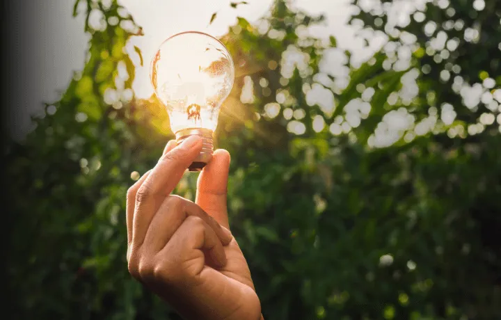 Mão segurando lâmpada acesa ao ar livre, simbolizando energia limpa e sustentabilidade
