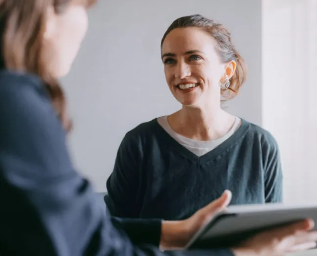 Duas mulheres conversando, com uma delas segurando um tablet