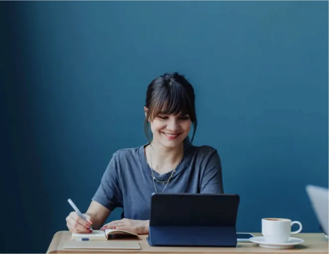 Mulher sorrindo enquanto trabalha no computador, representando a satisfação e segurança proporcionadas pela adesão à previdência empresarial oferecida pela empresa.