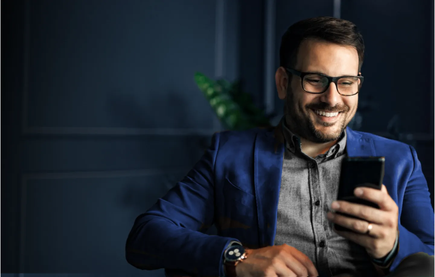 Homem sentado, sorrindo serenamente enquanto olha para o celular,simbolizando segurança e planejamento financeiro