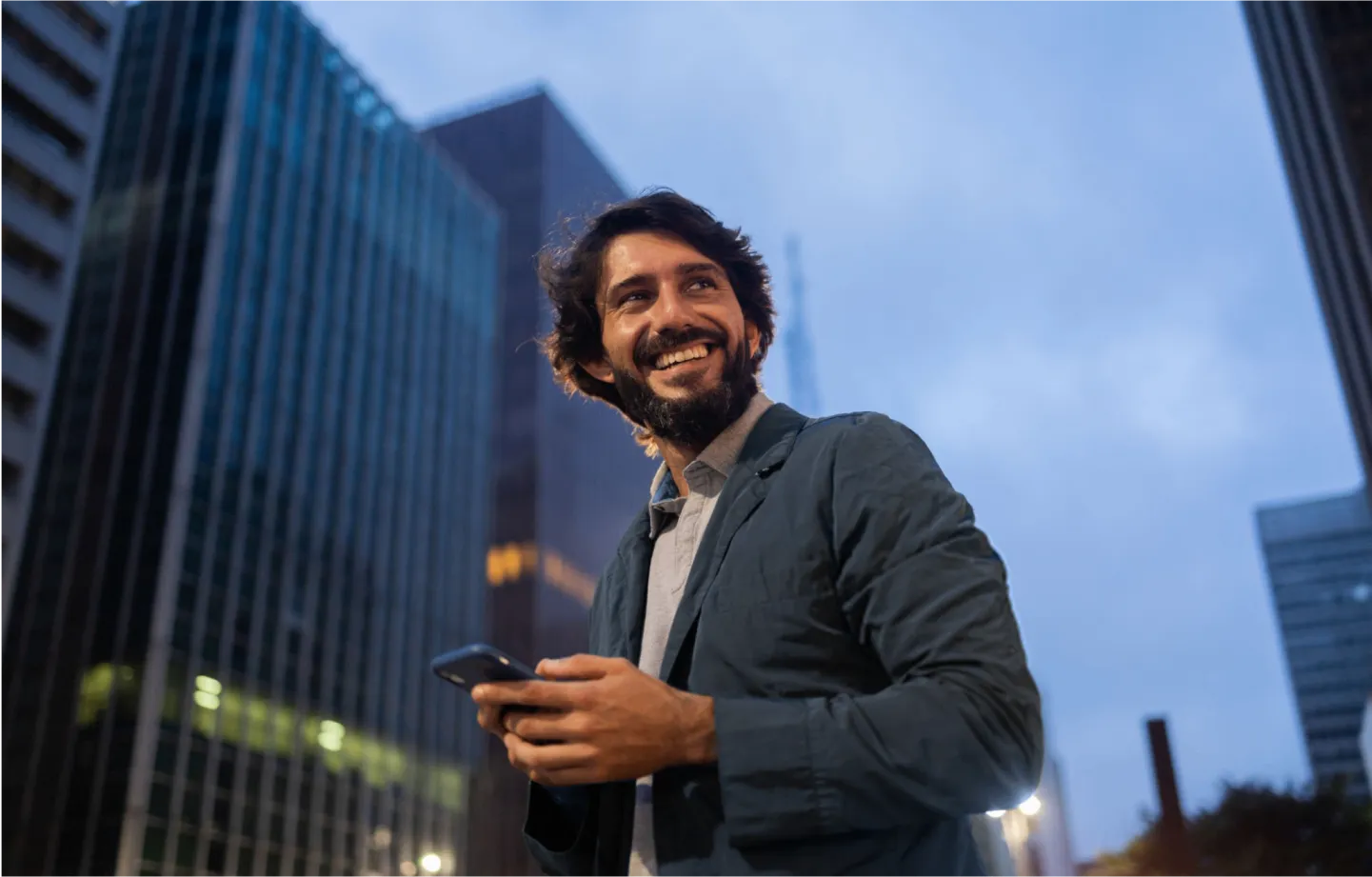 homem em ambiente externo sorrindo com celular em mãos olhando para o horizonte