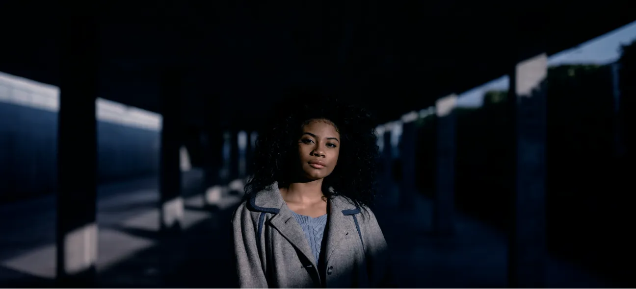 mulher em ambiente interno escuro com a luz em foco no seu rosto e busto