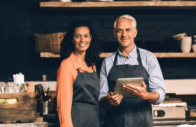 Um casal de empreendedores com aventais, em frente ao seu negócio, transmitindo segurança e confiança na proteção oferecida pelo seguro para empresas.