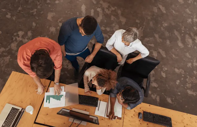 Vista aérea de um grupo de pessoas colaborando em uma mesa de trabalho, representando a abordagem digital e colaborativa da TIBI Seguros na oferta de seguros empresariais.