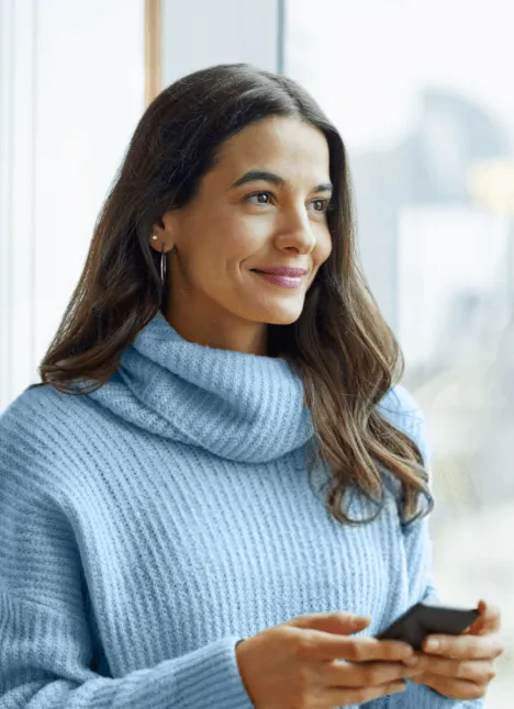 Uma mulher empresária olhando pela janela com uma expressão serena, transmitindo a tranquilidade que o seguro empresarial proporciona.