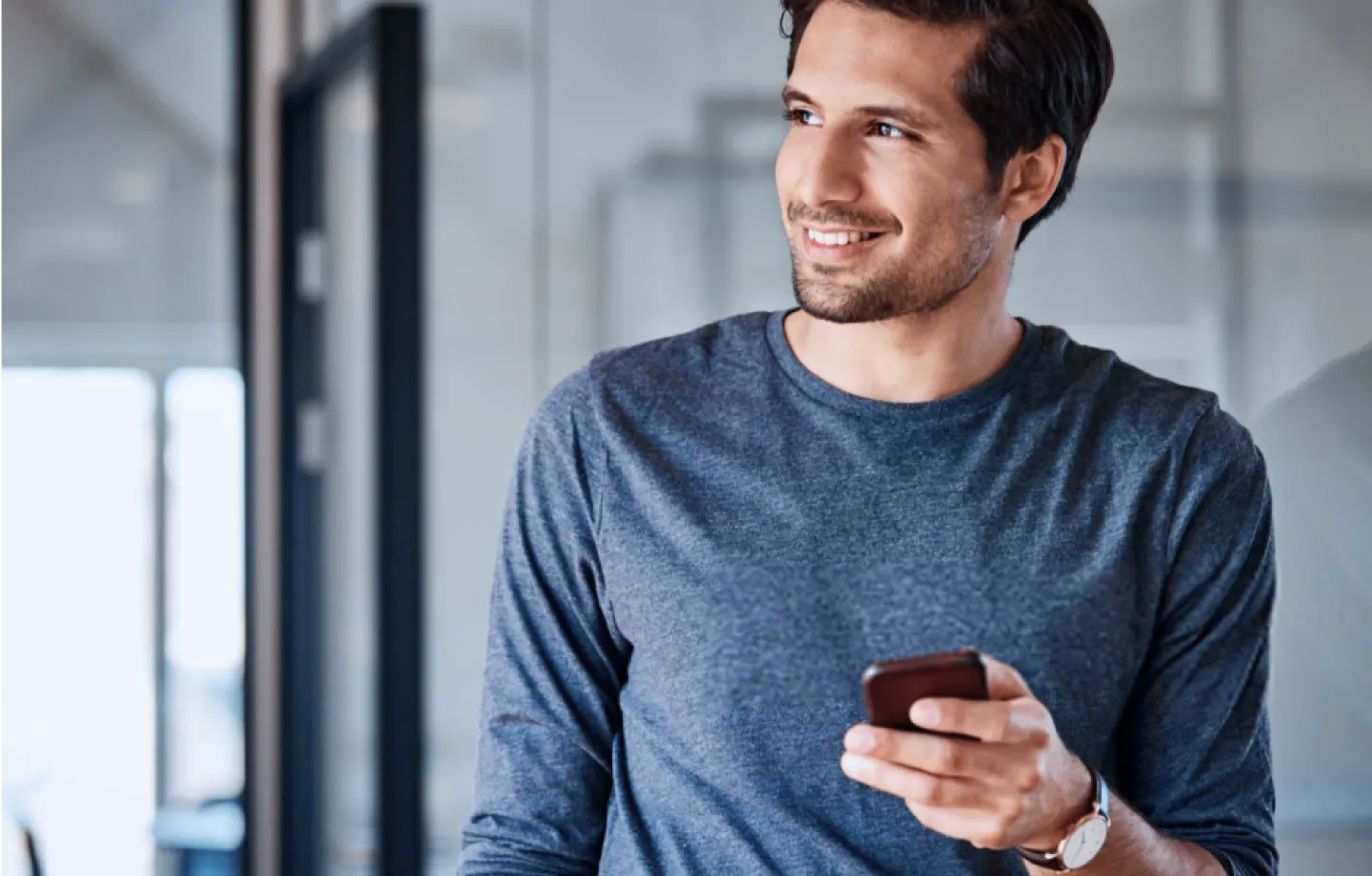 Homem sorrindo tranquilamente enquanto segura um celular e olha pela janela,representando confiança na antecipação