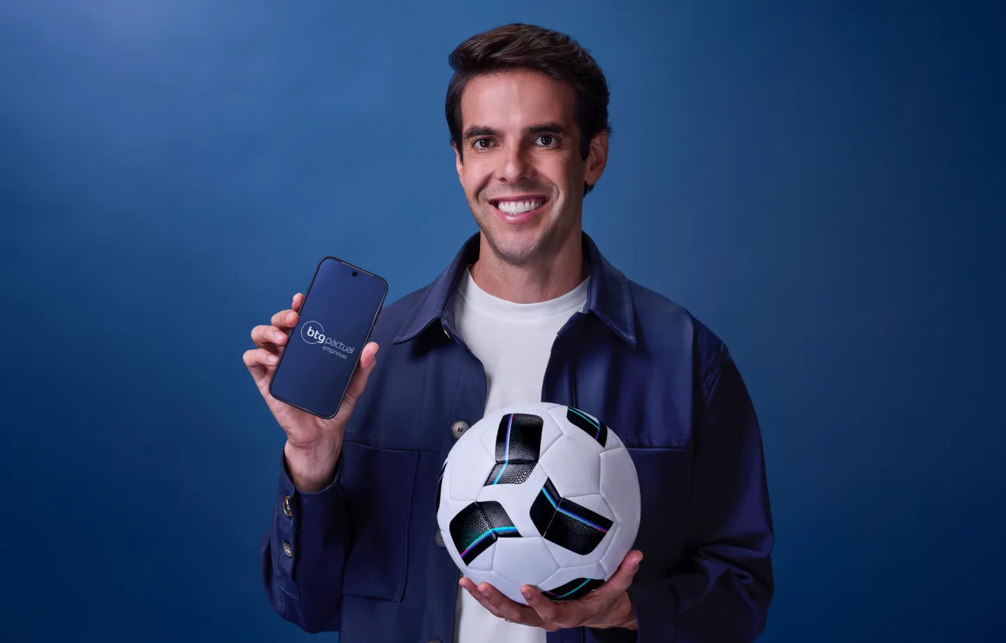 Kaká segurando smartphone e bola de futebol, promovendo aplicativo do BTG Pactual Empresas.